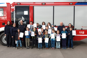 Eine Kindergruppe steht umringt von den Prüfern vor einen Feuerwehrfahrzeug.