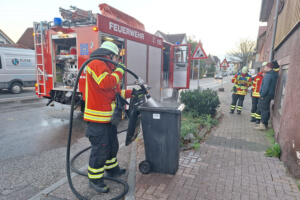 Ein feuerwehrmann löscht eine rauchende Mülltonne.